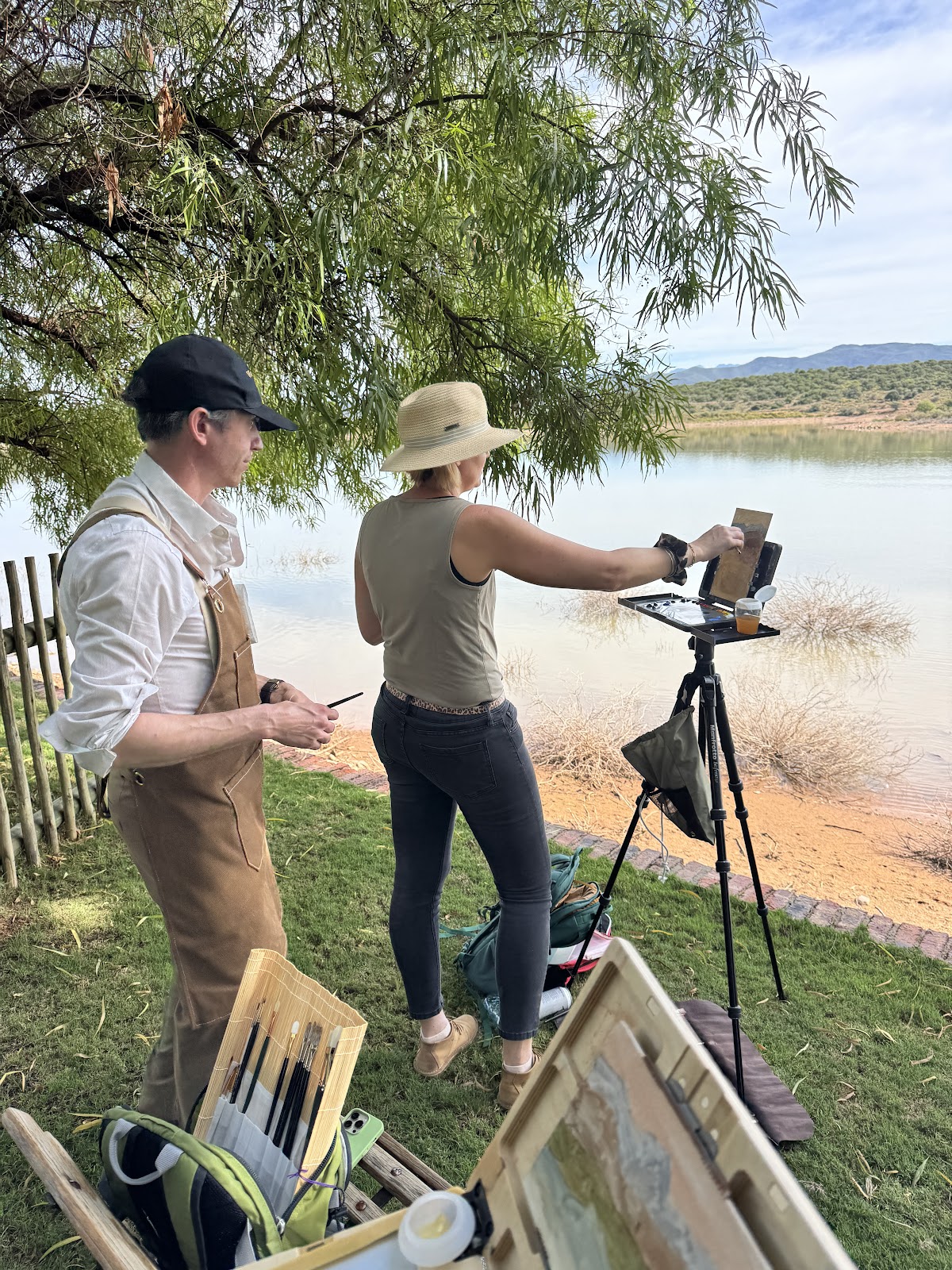 An artist receiving plein-air painting guidance beside a calm African lake