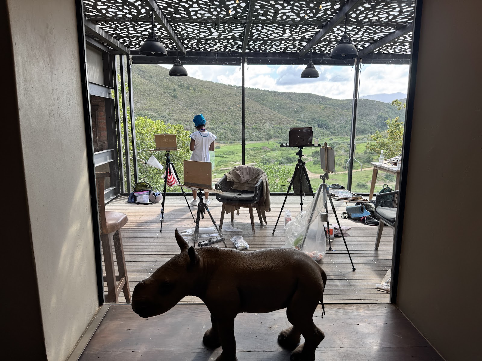 A hippo silhouette in front of an open-air painting setup overlooking the landscape