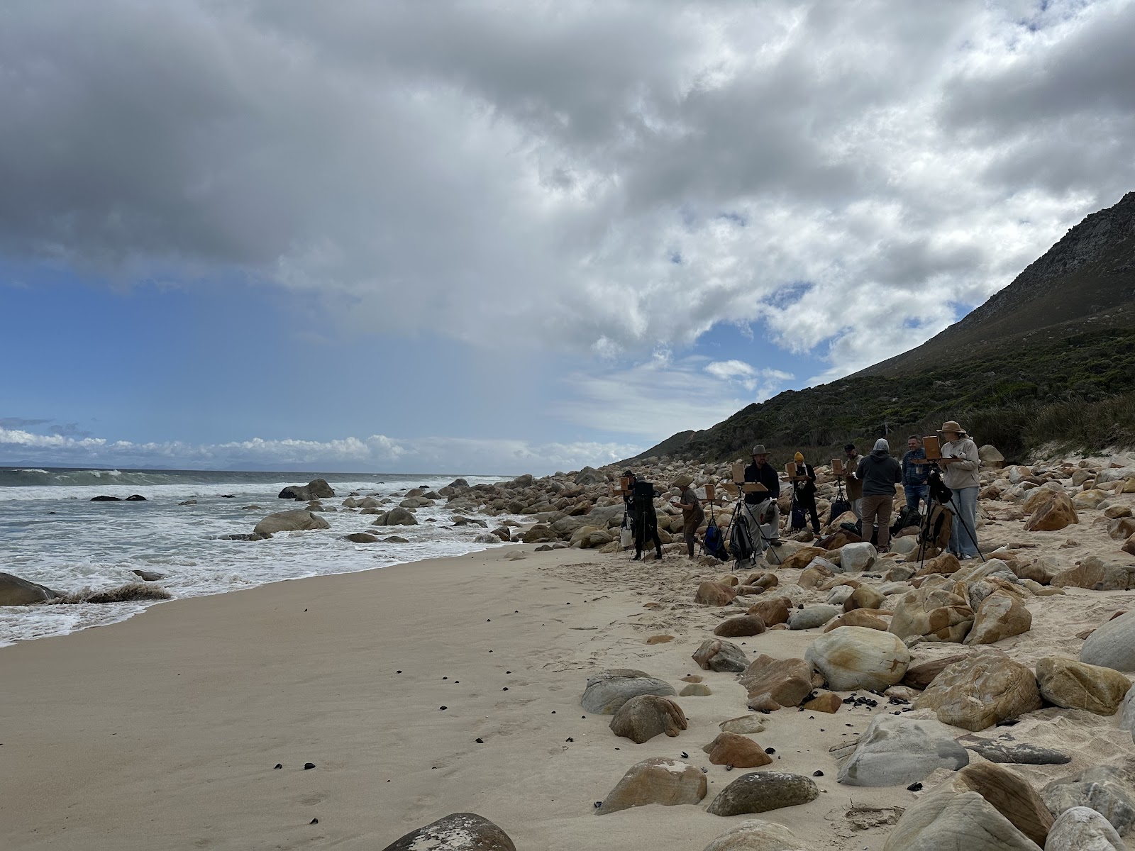 Workshop artists painting together on a rocky Cape beach in a photograph by Raegan Brown